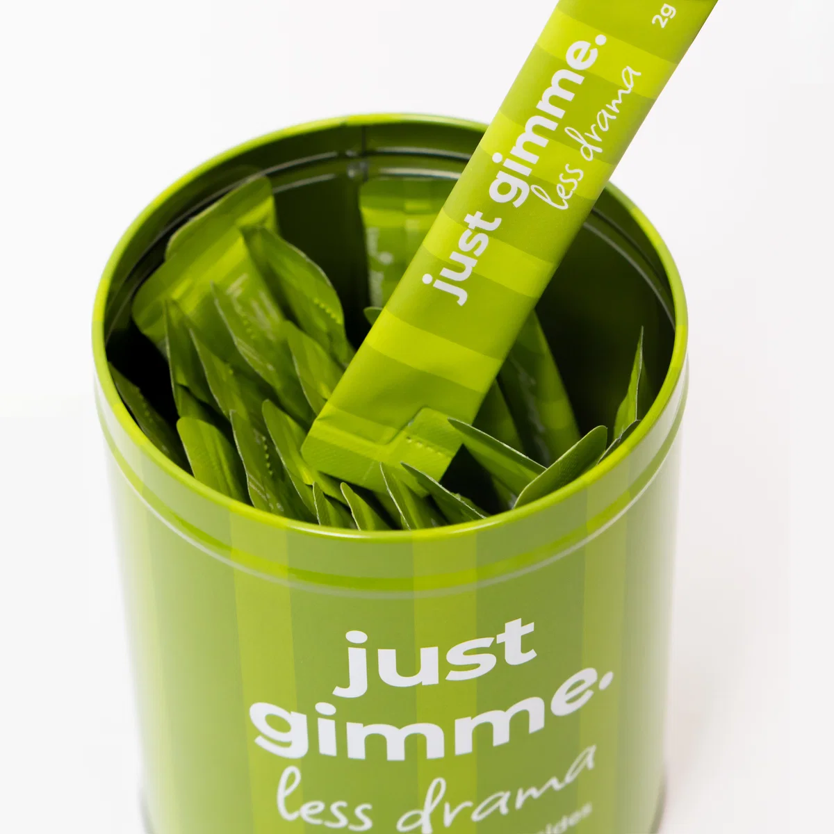 11_c7026da9-c4ea-4c0f-82cf-e214a61288fd Green tin filled with stacked leaf-shaped tea sachets and a matching green scoop labeled 'just gimme less drama'